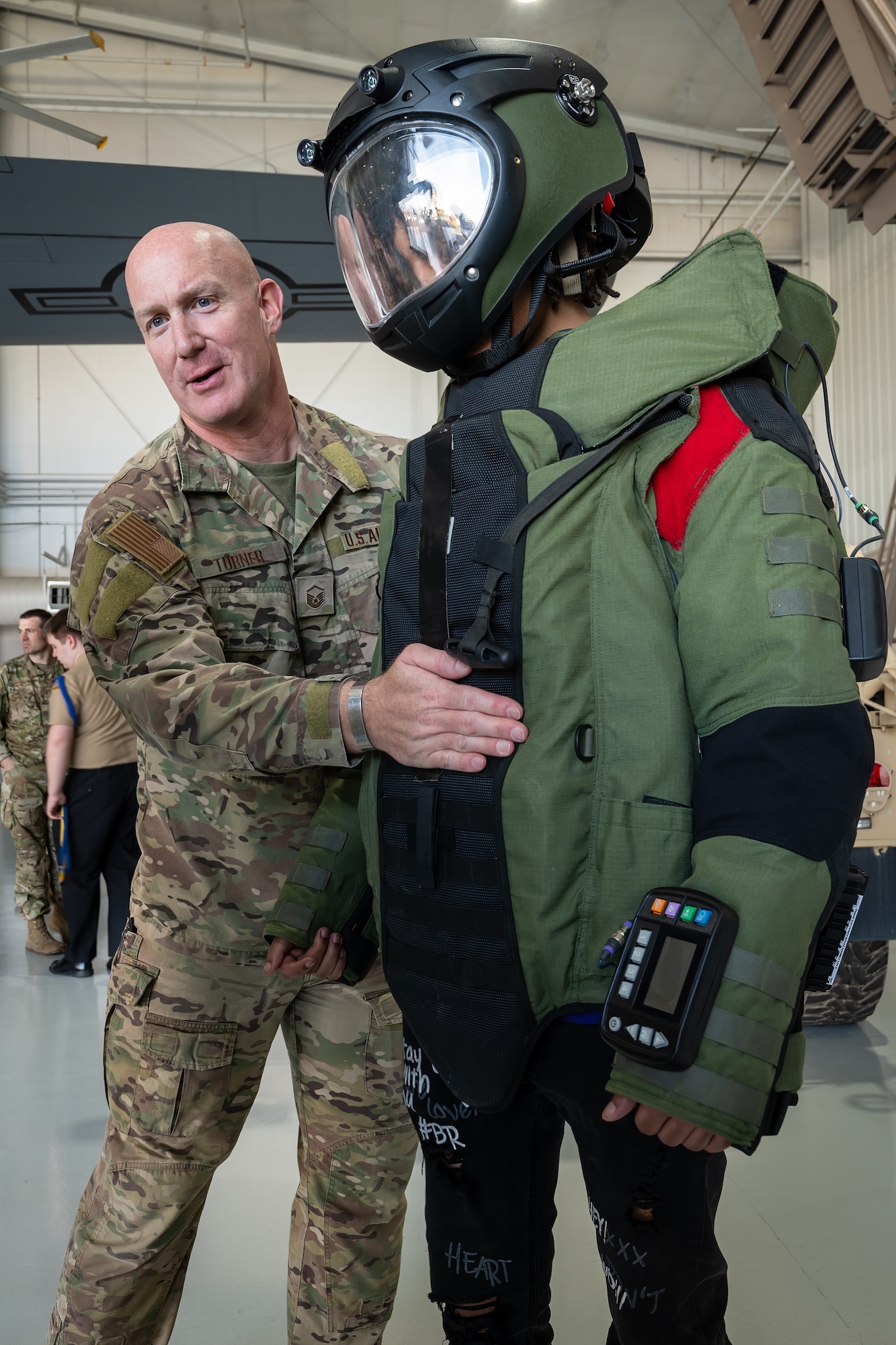 Master Sgt. Dustin Turner, an explosive ordnance disposal specialist assigned to the 123rd Airlift Wing, helps a student from Shawnee High School’s Navy JROTC program don a protective bomb suit at the Kentucky Air National Guard Base in Louisville, Ky., March 14, 2024. The base is home to about 1,200 Airmen and eight C-130J Super Hercules aircraft, with missions spanning the gamut from tactical airlift, special operations, disaster response, explosive ordnance disposal and aircraft maintenance to civil engineering, cyber communications, security forces, medical care and logistics. (U.S. Air National Guard photo by Dale Greer)