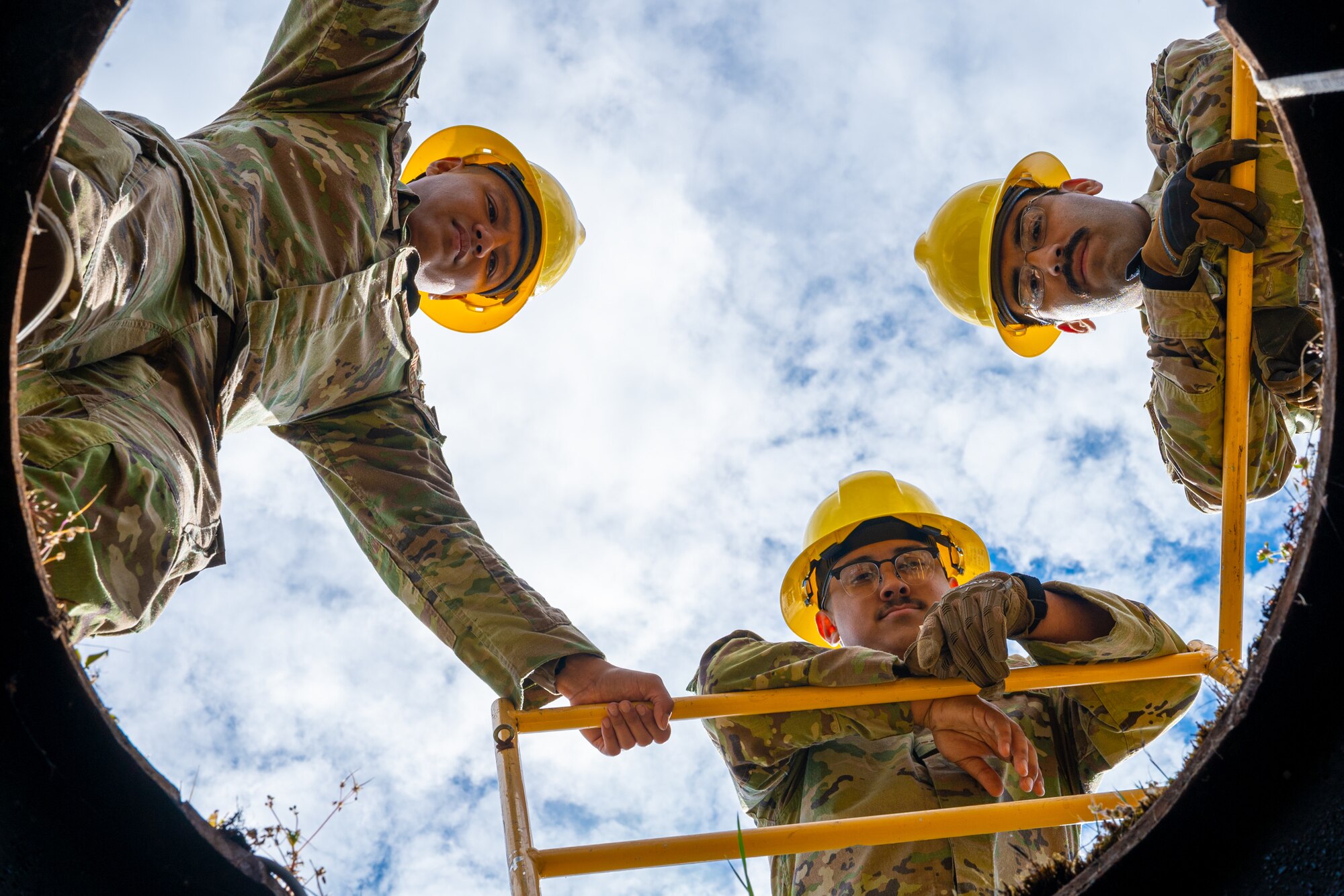 U.S. Air Force Staff Sgt. Christian Apatang, a cable and antenna systems technician supervisor with the 627th Communications Squadron, left, Airman 1st Class Rogelio Alvarez, middle, and Senior Airman Hector Salinas, cable and antenna systems technicians with the 627th CS, look down a manhole at Joint Base Lewis-McChord, Washington, May 28, 2024. Cable and antenna systems Airmen work closely to ensure safety procedures are met and assist each other during operations. (U.S. Air Force photo by Airman 1st Class Benjamin Riddle)