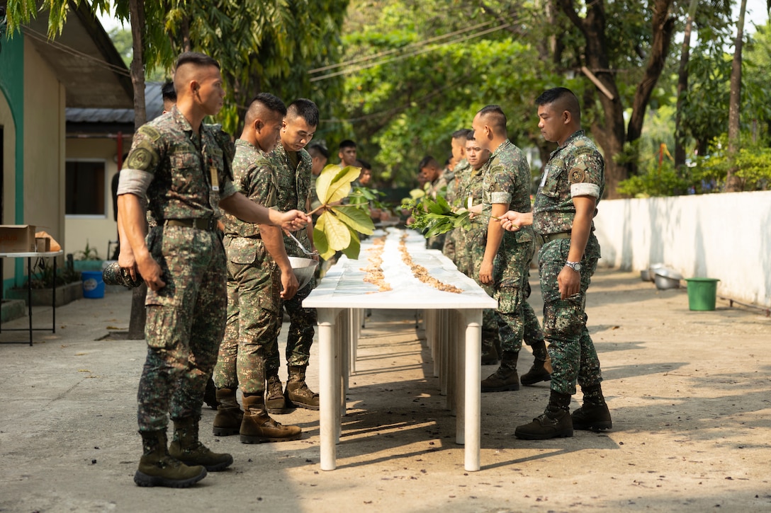 U.S. Marines and Sailors with Marine Wing Support Squadron (MWSS) 371, Marine Air Control Group 38, 3rd Marine Aircraft Wing; Marine Aircraft Group 13, 3rd MAW, and Philippine Marines hold a boodle fight during Marine Aviation Support Activity 24 at Fort Bonifacio, Manila, Philippines, June 13, 2024. A boodle fight is a tradition of the Armed Forces of the Philippines where participants eat with their hands from a feast in order to build camaraderie regardless of rank. MASA is an annual Philippine-U.S. military exercise focused on mutual defense, strengthening relationships, and rehearsing emerging aviation concepts. (U.S. Marine Corps photo by Cpl. Kayla Halloran)
