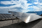 A line of solar panels reflect the sun on a partly cloudy day.