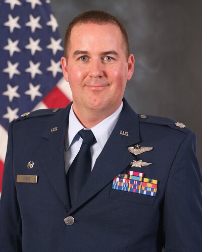 photo of uniformed U.S. Air Force Airman standing in front of U.S. flag.