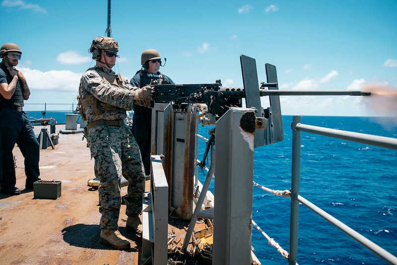 Three military men shooting a weapon attached to a ship