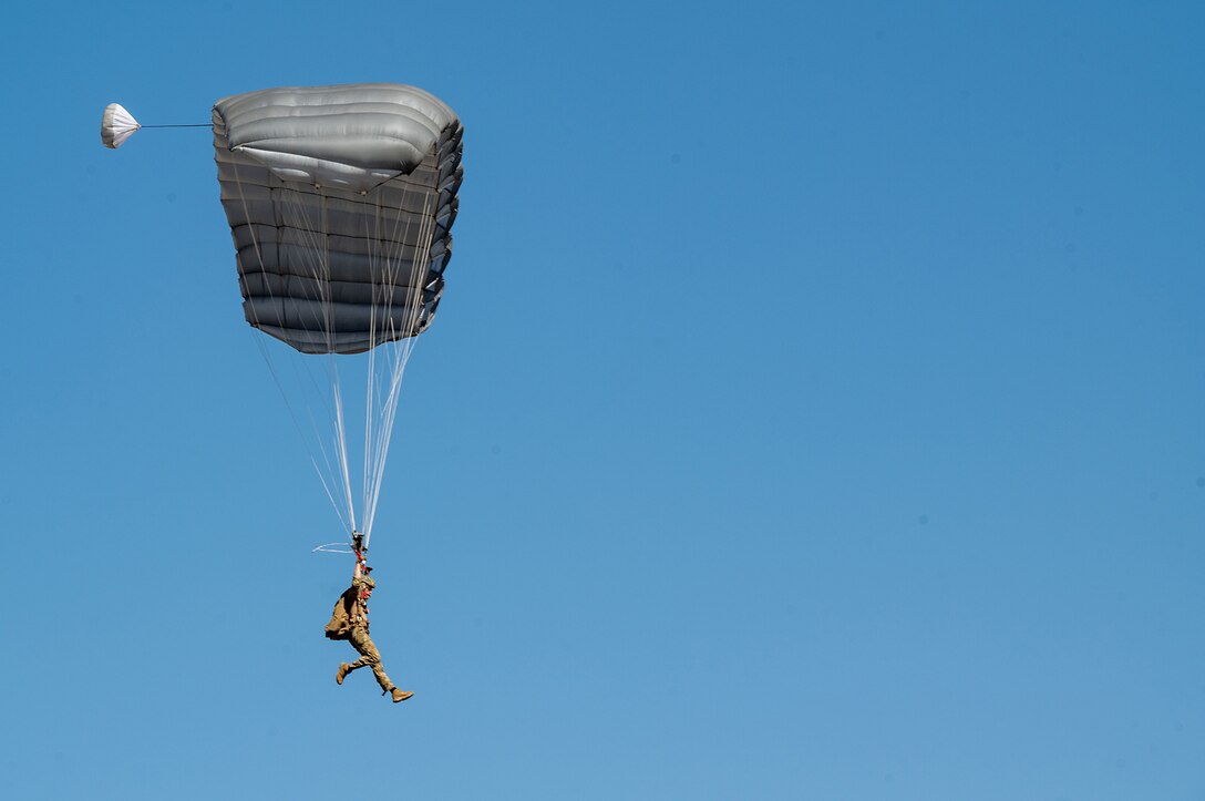 A soldier parachutes during free-fall training against a bright blue sky.