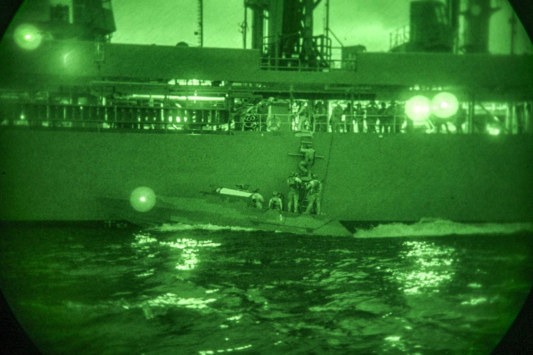 Sailors are viewed from a scope, boarding a ship from a small boat. They are illuminated by green light.