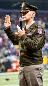 Man wearing Army dress uniform holds right hand with microphone.