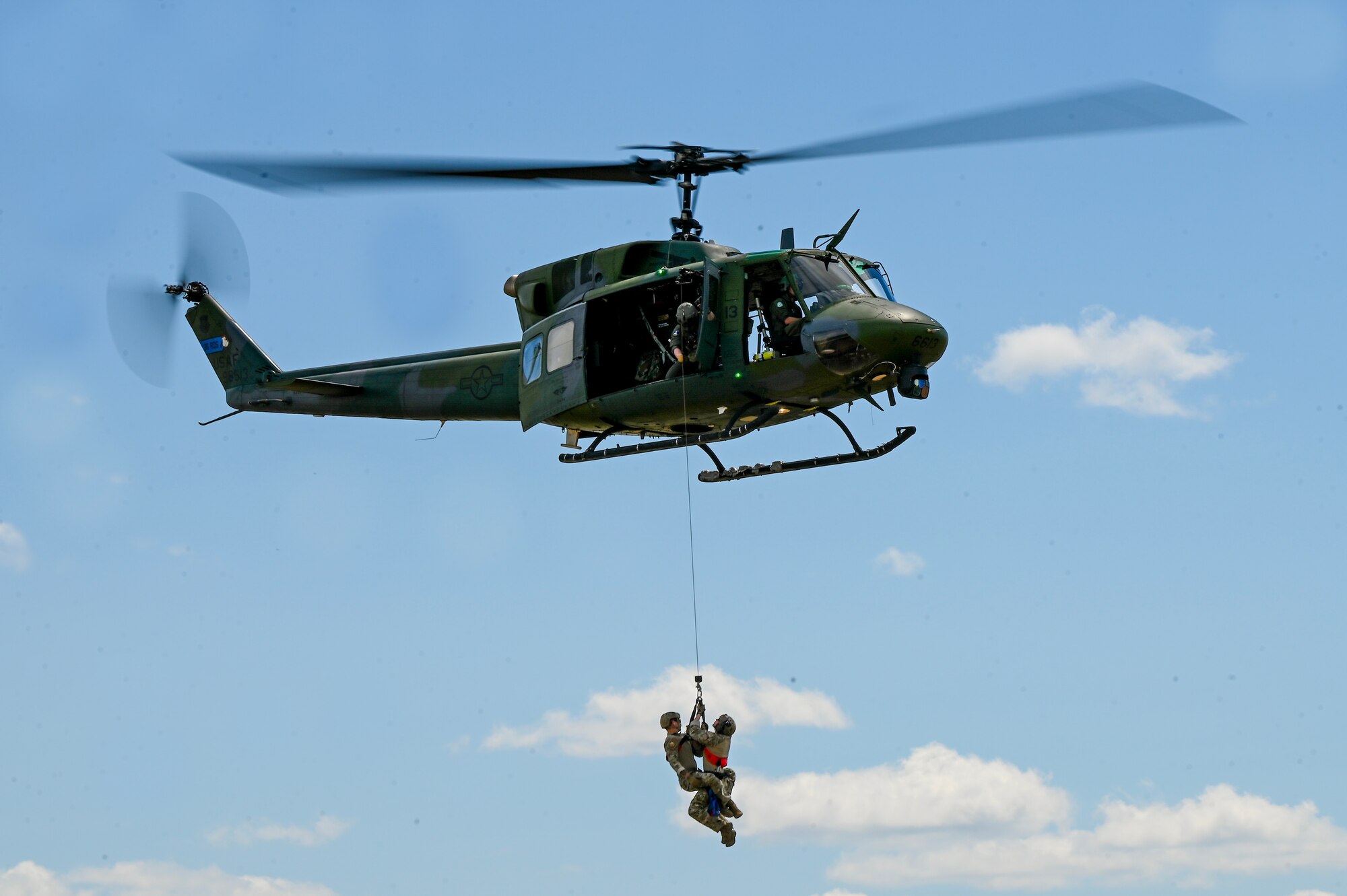 A UH-1N helicoptor hoists up Airmen.