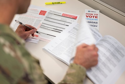 A service member turns the page of a book on a desk while holding a pen.