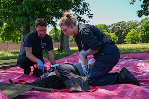 Two EMTs performing medical care on a patient on a pink tarp.
