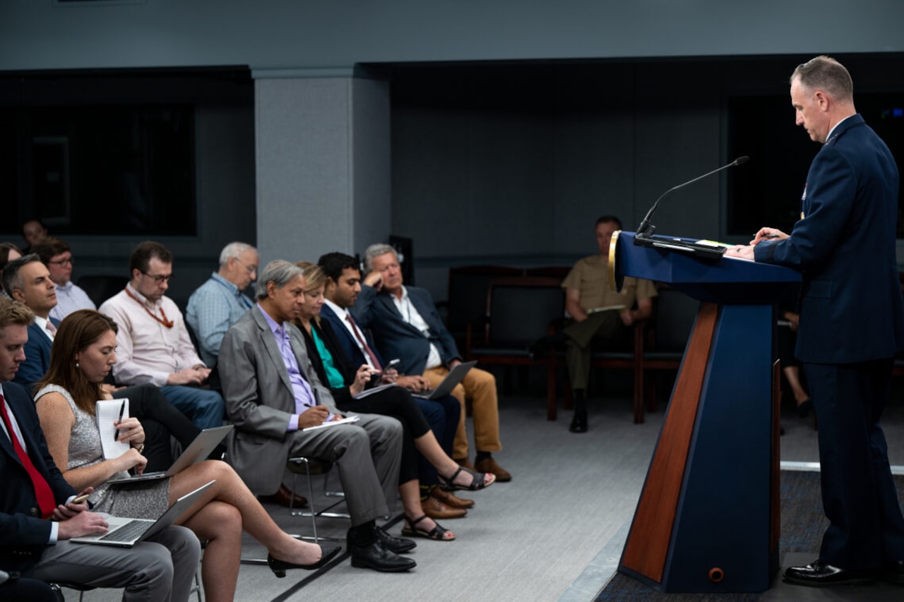 A man stands at a podium facing a small group of people.