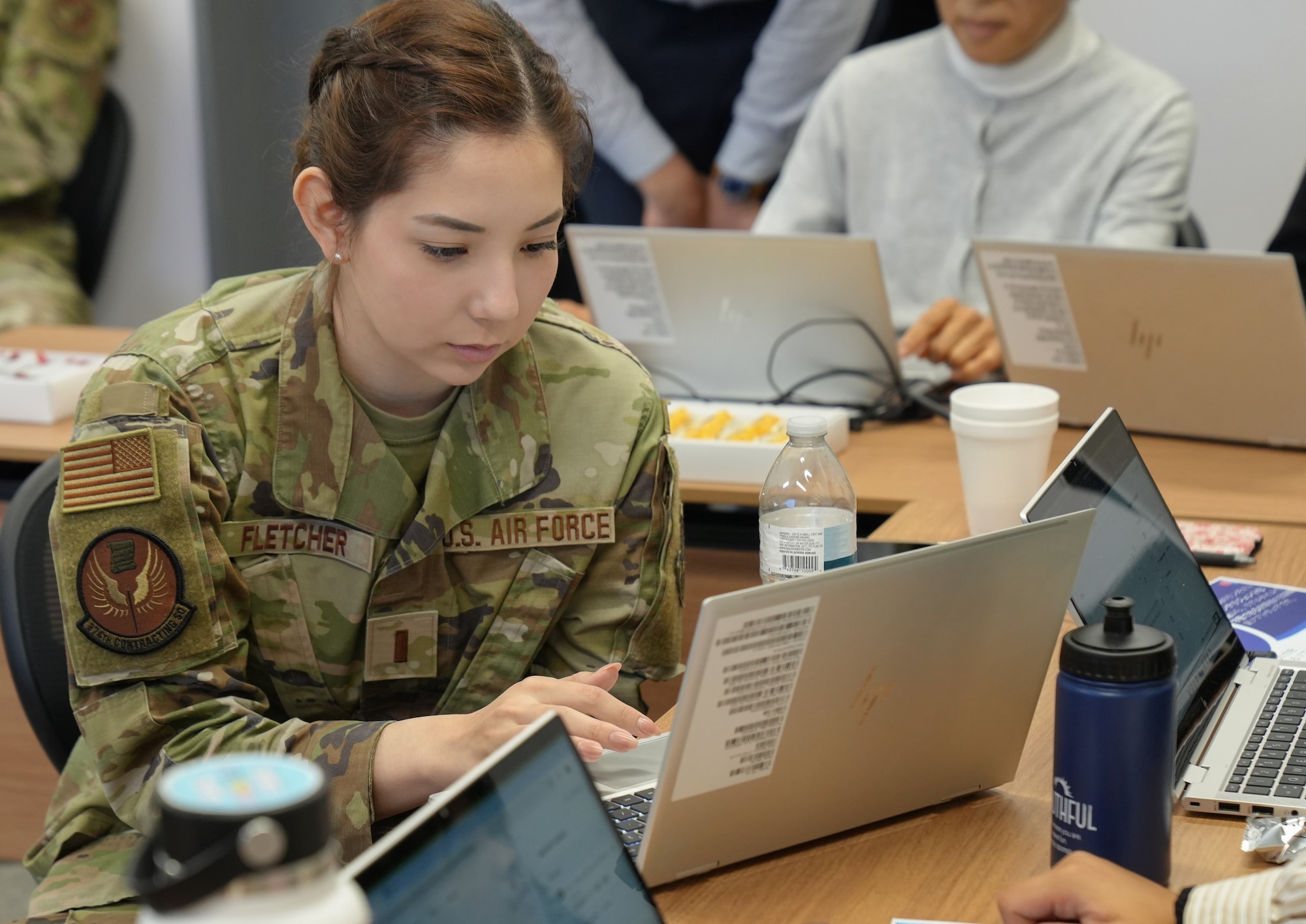 A young uniformed woman types on a laptop.