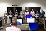 Eight people standing at front of room holding certificates.