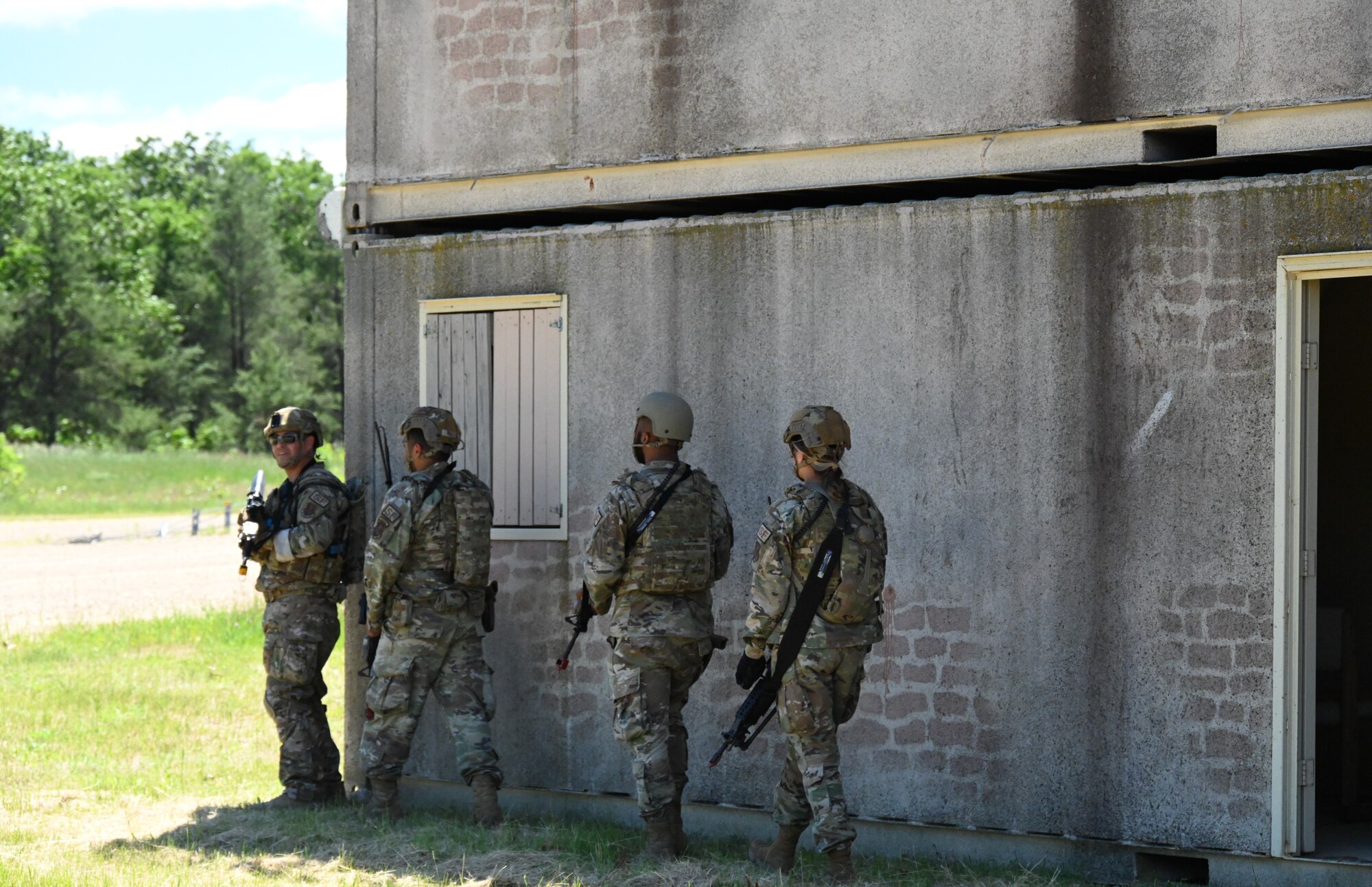 Four Air Force members with simulated weapons stand beside brick building.
