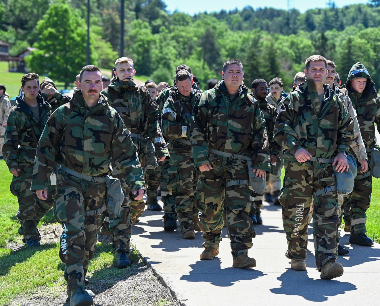 Airmen in chemical gear walk down a sidewalk.