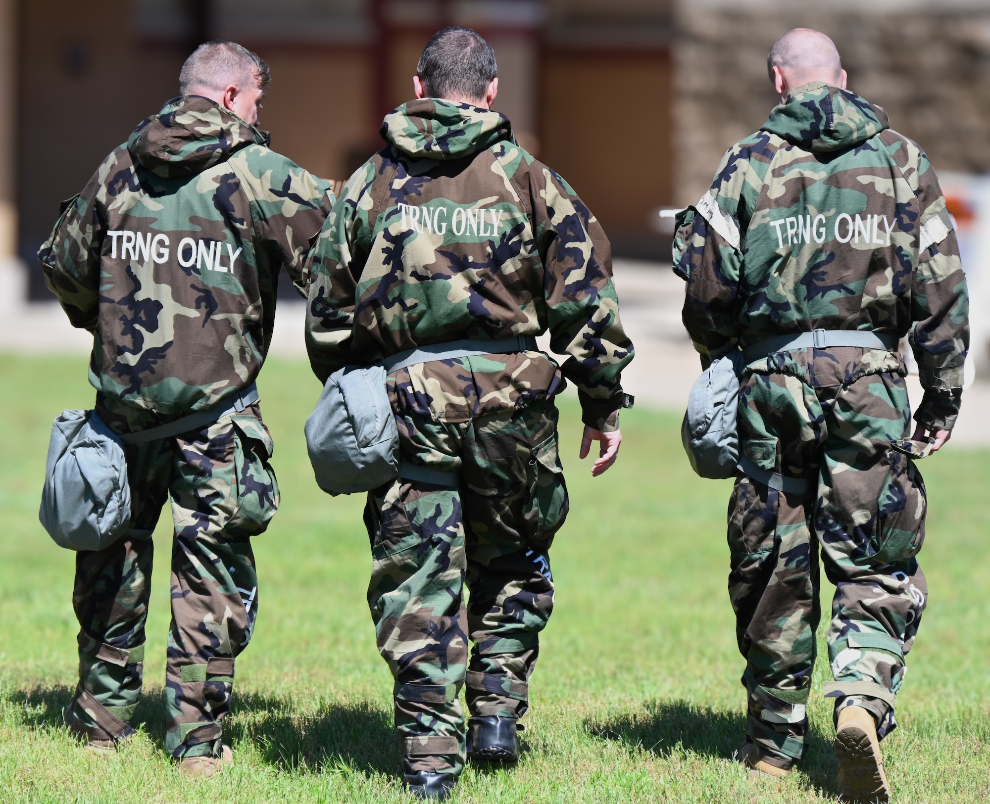 Three Airmen walking away in chemical training gear.