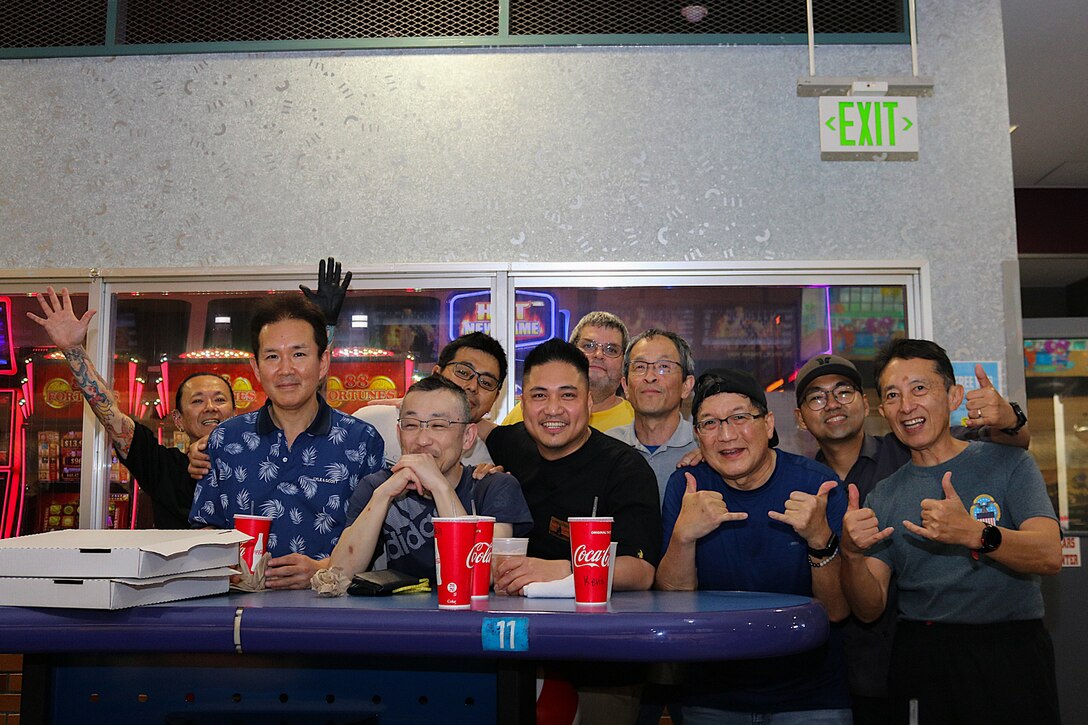 A group of 10 people pose for a group photo behind a table in a bowling alley.