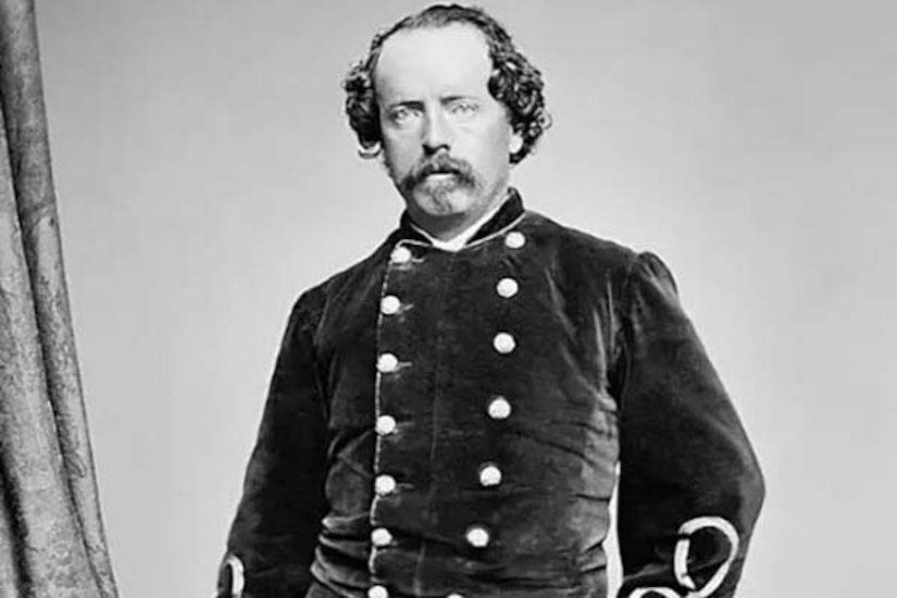 A man in uniform and holding white gloves poses for a photo.