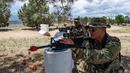 Two service members with training rifles leaning against a barrier.