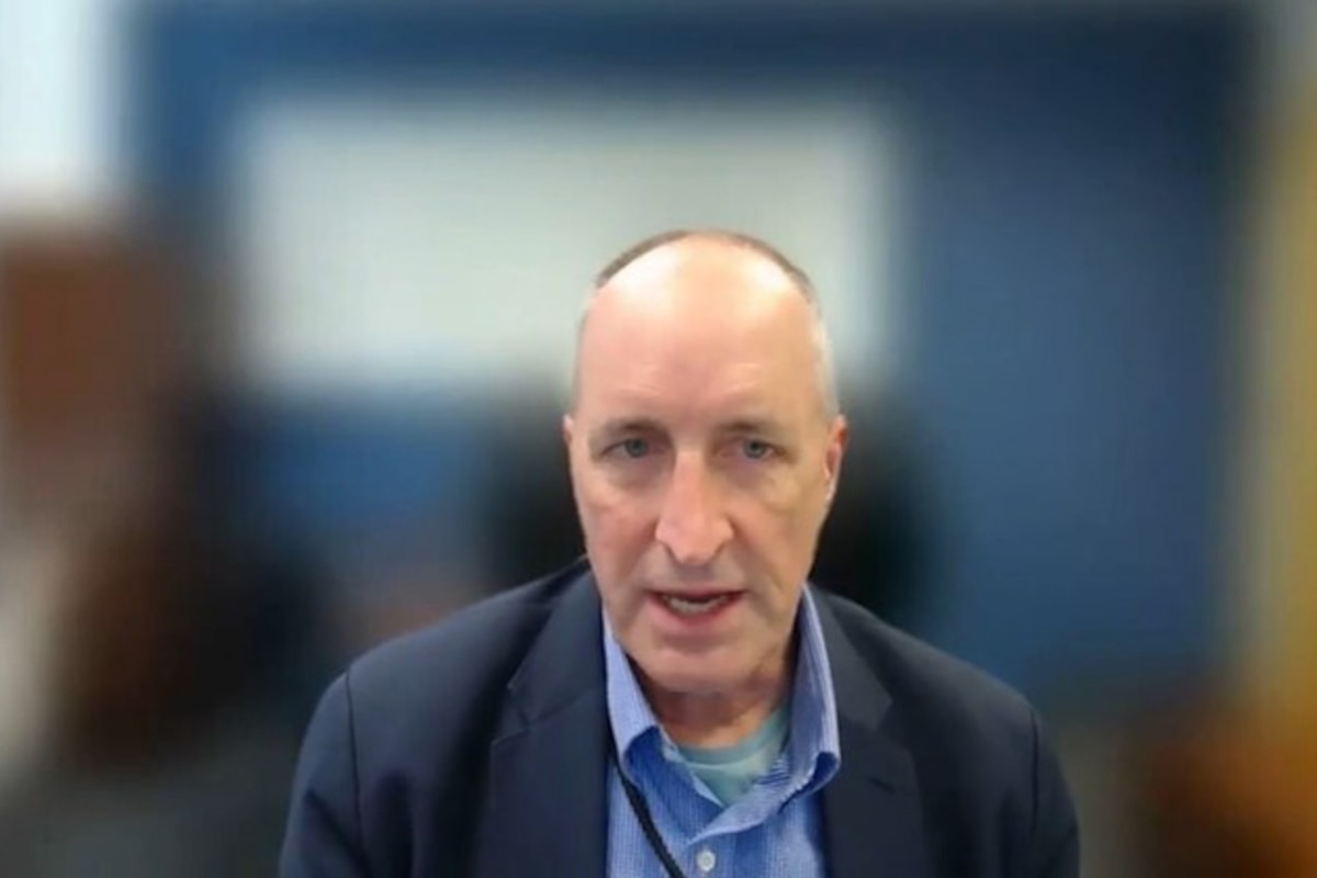 A speaker wearing a suit speaks into the camera with a blurred background.