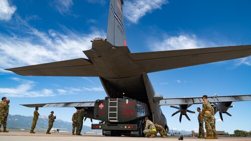 A truck being loaded into the bay of an aircraft surrounded by a crew of servicemembers.