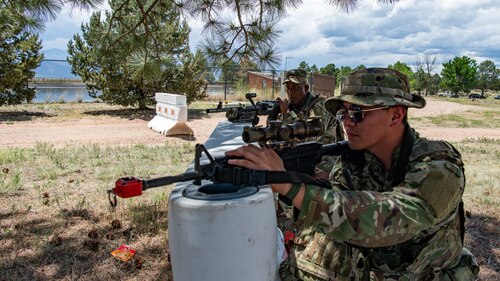Two service members with training rifles leaning against a barrier.