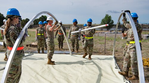 A team of servicemembers holding and assembling components to a tent.