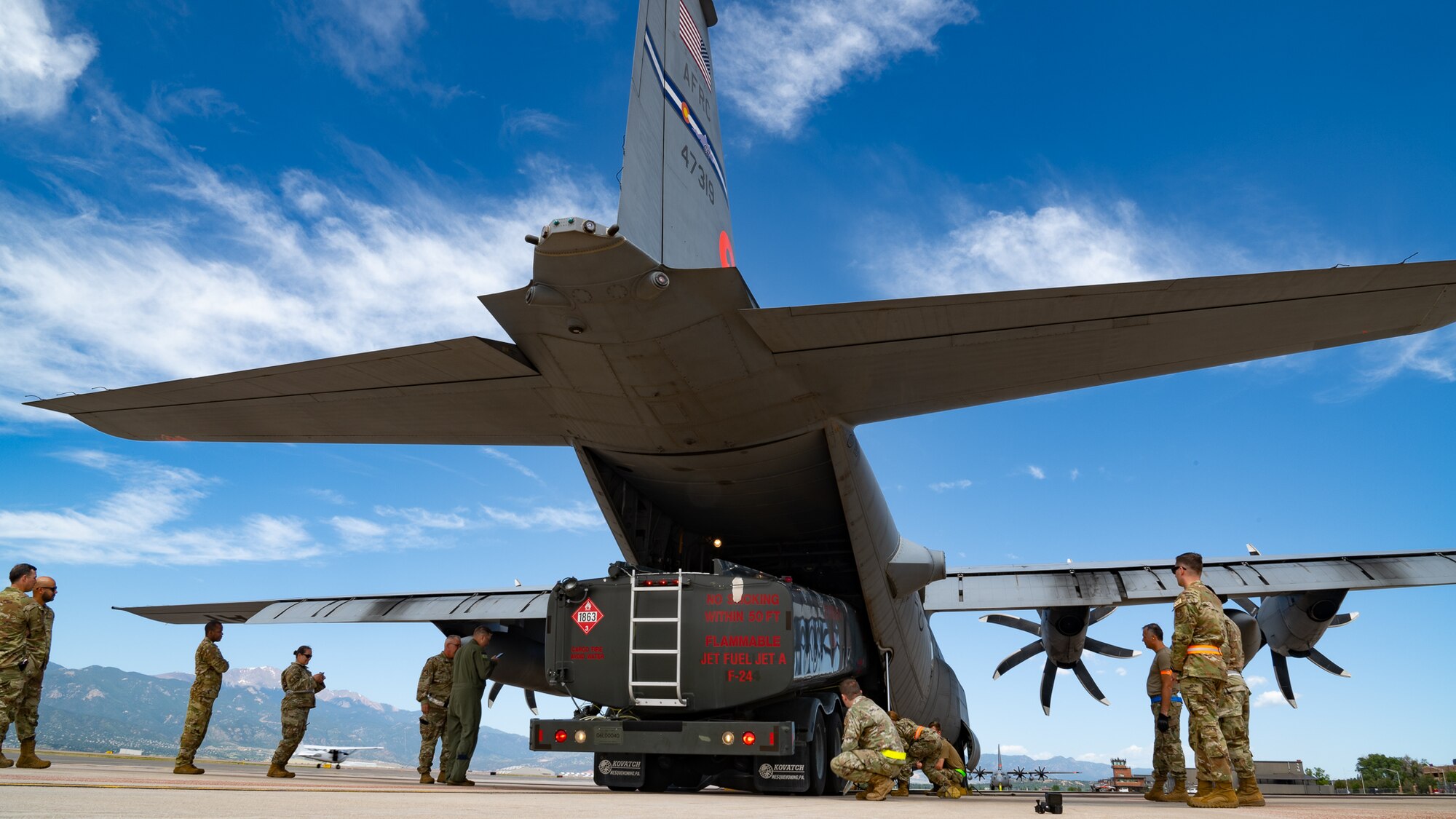 A truck being loaded into the bay of an aircraft surrounded by a crew of servicemembers.