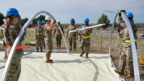 A team of servicemembers holding and assembling components to a tent.
