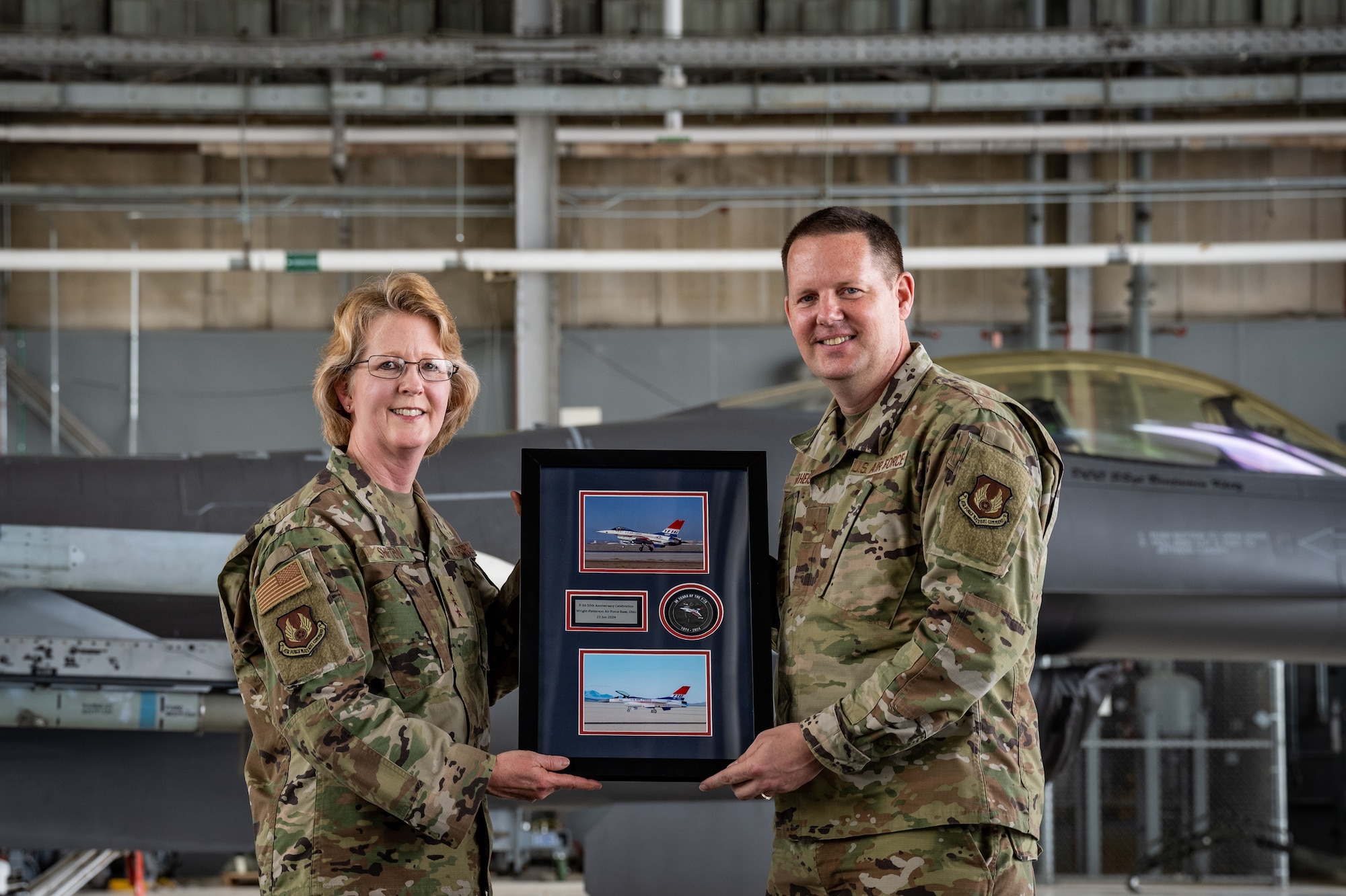 Two USAF generals stand on stage, holding a plaque to commemorate the F-16 50th anniversary.
