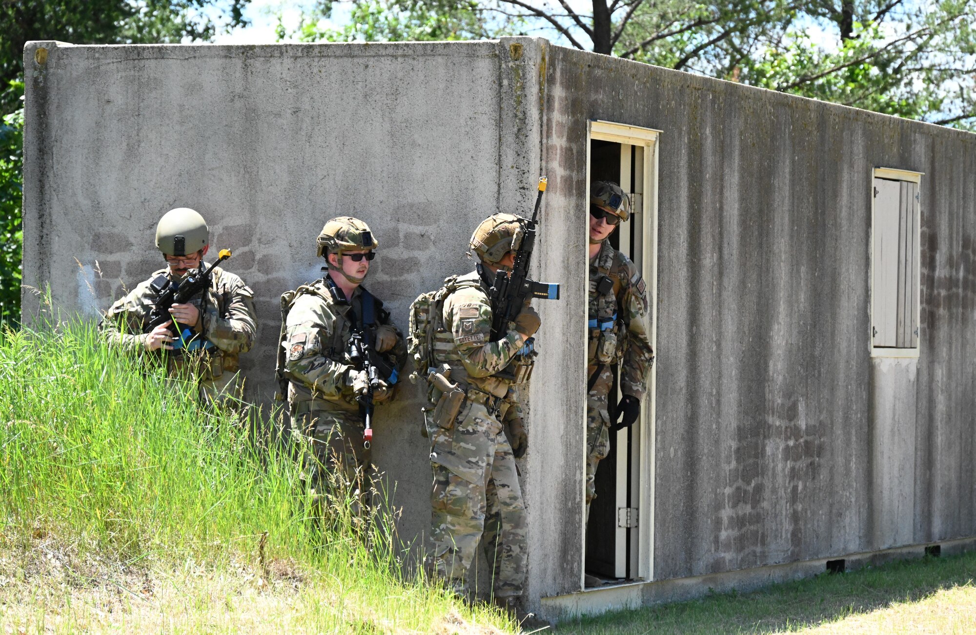 Armed Air Force members simulate clearing a brick building while holding weapons.