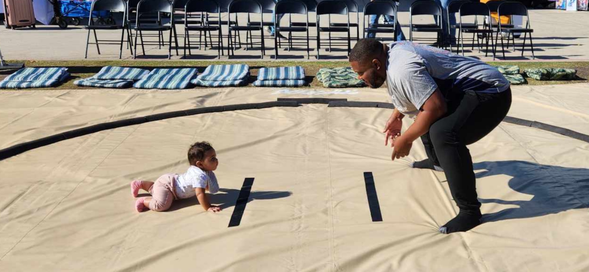 Scriven, at right, squats in the sumo position while his infant daughter crawls toward him in a sumo ring.