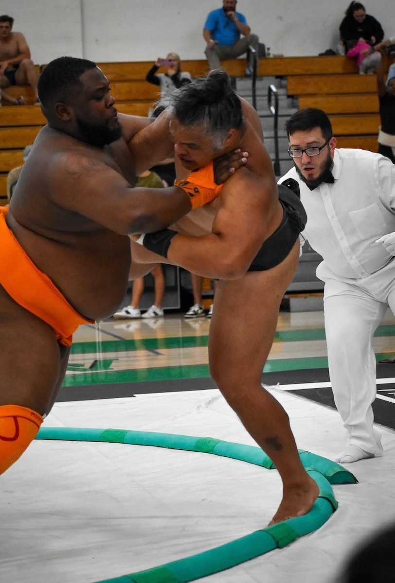 Closeup of Scriven pushing against Huynh as Huynh tries to brace his foot against the edge of the ring. Referee looks on.