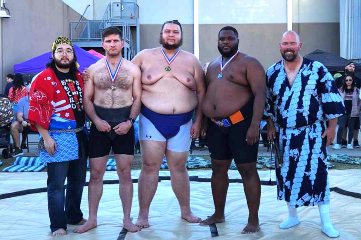 Group photo of five people in a sumo ring with three wearing their Texas State Classic medals around their necks.