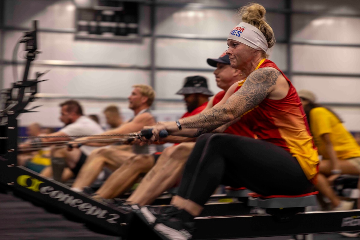 A group of athletes focus as they use indoor rowing machines in a gym.