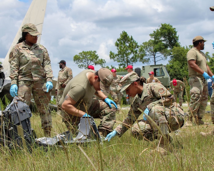 Airmen crouched down and searching a field for debris following a simulated crash.