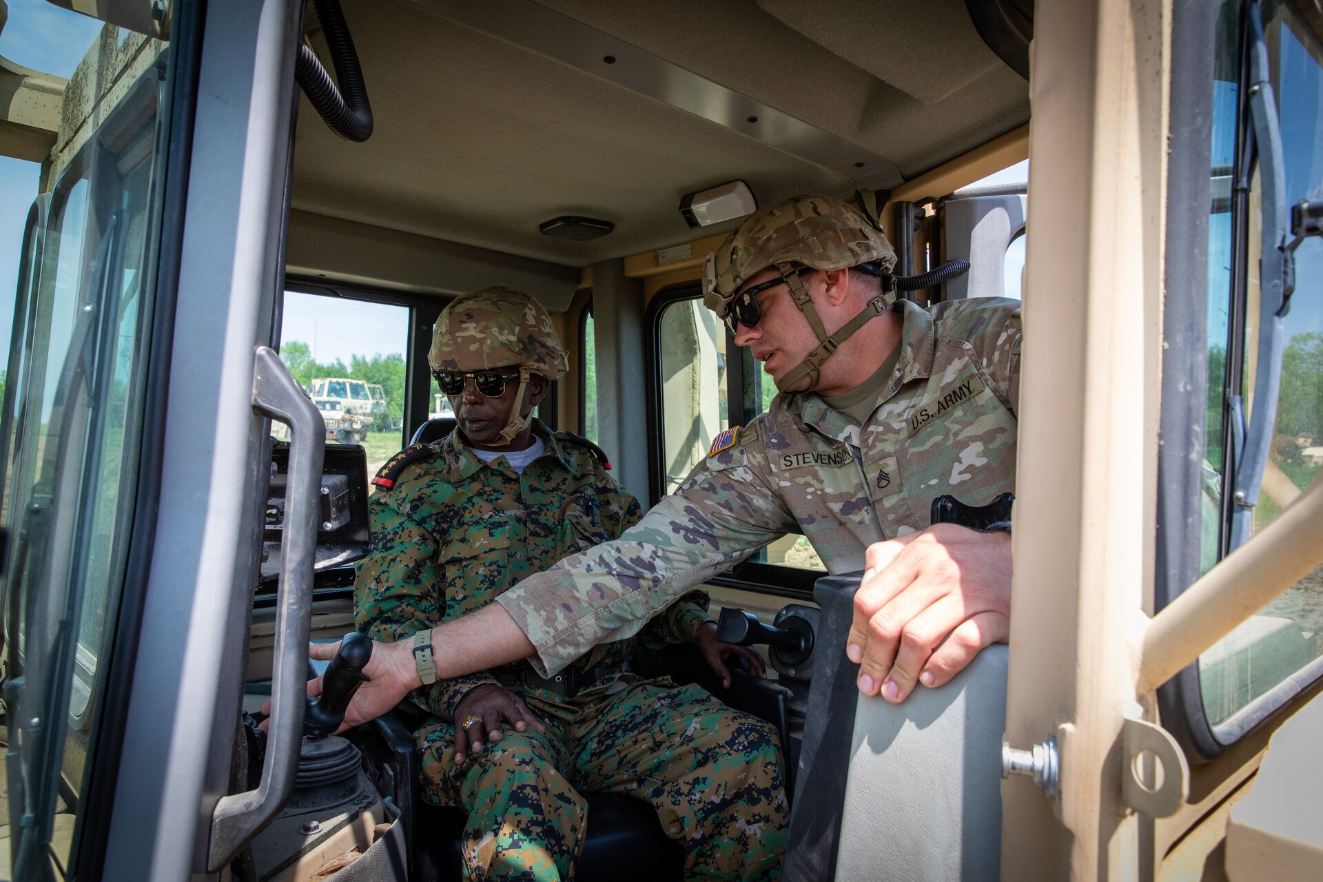 U.S. Army Staff Sgt. Logan Stevenson, a squad leader with the 130th Engineer Support Company, demonstrates the operations of  a High Mobility Engineer Excavator (HMEE) to an engineer officer of the Djibouti Armed Forces (DAF) at Camp Dodge, Iowa on May 15, 2024. The DAF visited the Kentucky Army National Guard's 206th Engineer Battalion's annual training to learn ideas on how to set up battalion level engineer operations. (U.S. Army National Guard photo by Sgt. 1st Class Andrew Dickson)