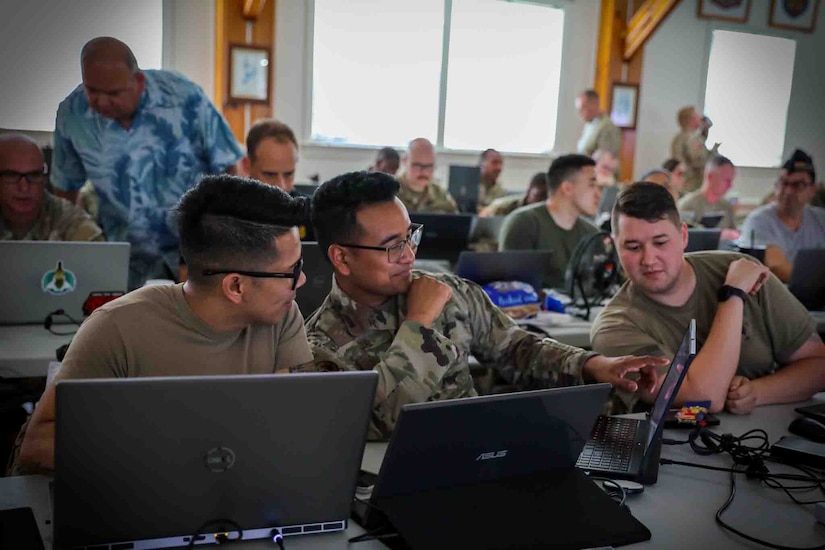 A large group of service members sit in front of laptop computers.