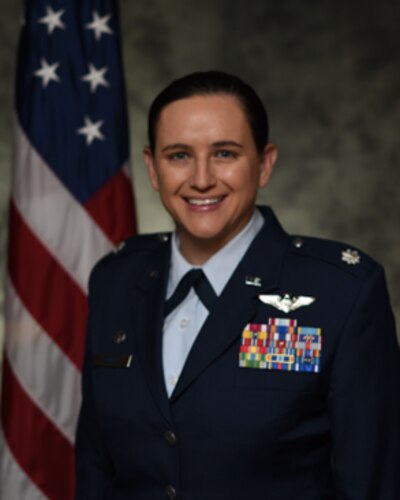 photo of uniformed U.S. Air Force Airman standing in front of a U.S. flag