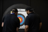 Miguel Avila watches as officials score his father, U.S. Army Cpt. Luis Avila's target during the archery event