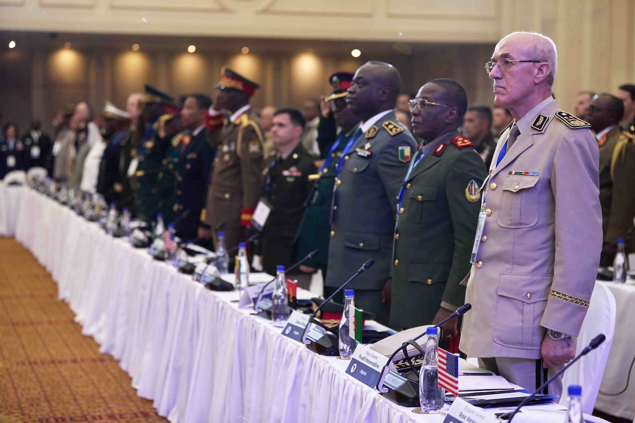 People in military and civilian attire stand in front of a long table.