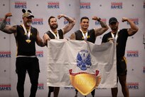 Team army indoor rowing gold medalists pose for a photo with the Army flag at the indoor rowing event