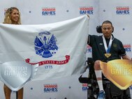 Team Army mentor Brandi Evans, left assists U.S. Army Cpt. Luis Avila hold up the Army flag after winning a gold medal at the precision air event