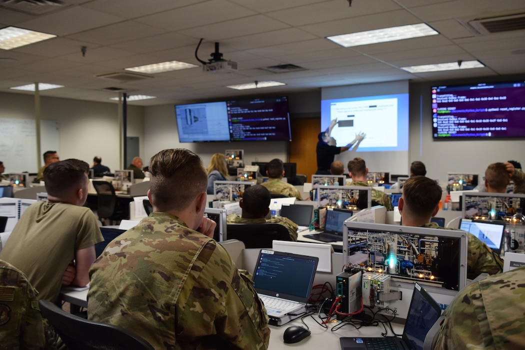 Men and women in green service uniforms sit in a classroom setting.