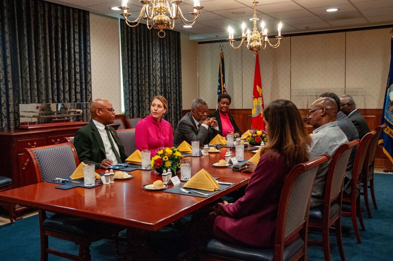 Civilians in business attire are seated around a table.