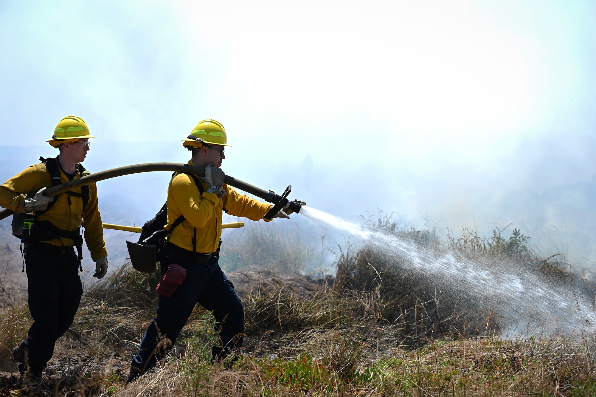 Two men put out a fire with water hose.