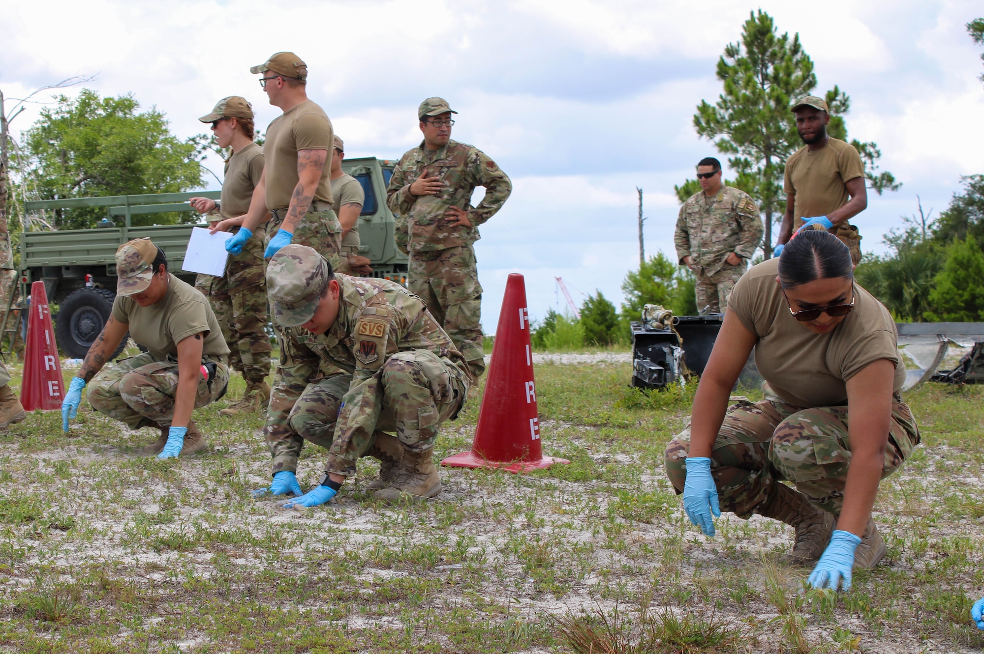 Airmen crouch down and search the ground for debris following a simulated crash.