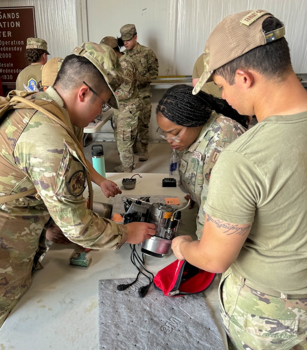 Four Airmen huddled around equipment on a work bench.