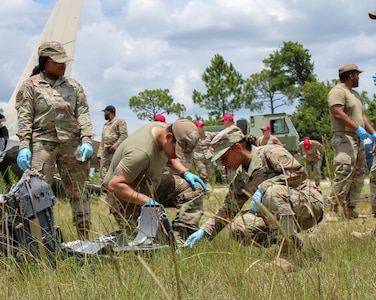 Airmen crouched down and searching a field for debris following a simulated crash.