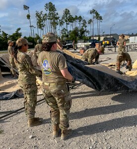 Two Airmen lift a side panel of a tent