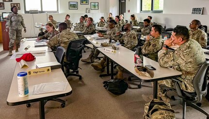 instructor at front of classroom with rows of students sitting at tables