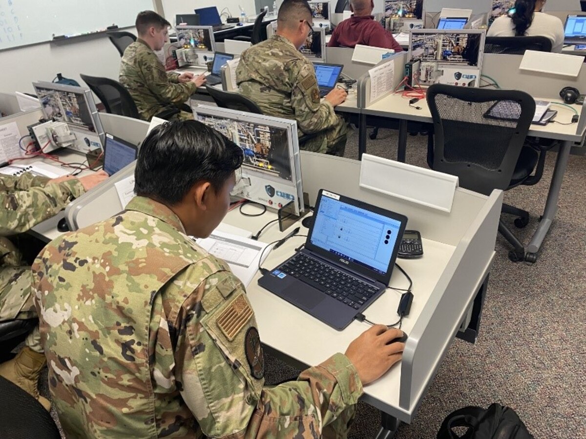 A man in a green service uniform works on a laptop.